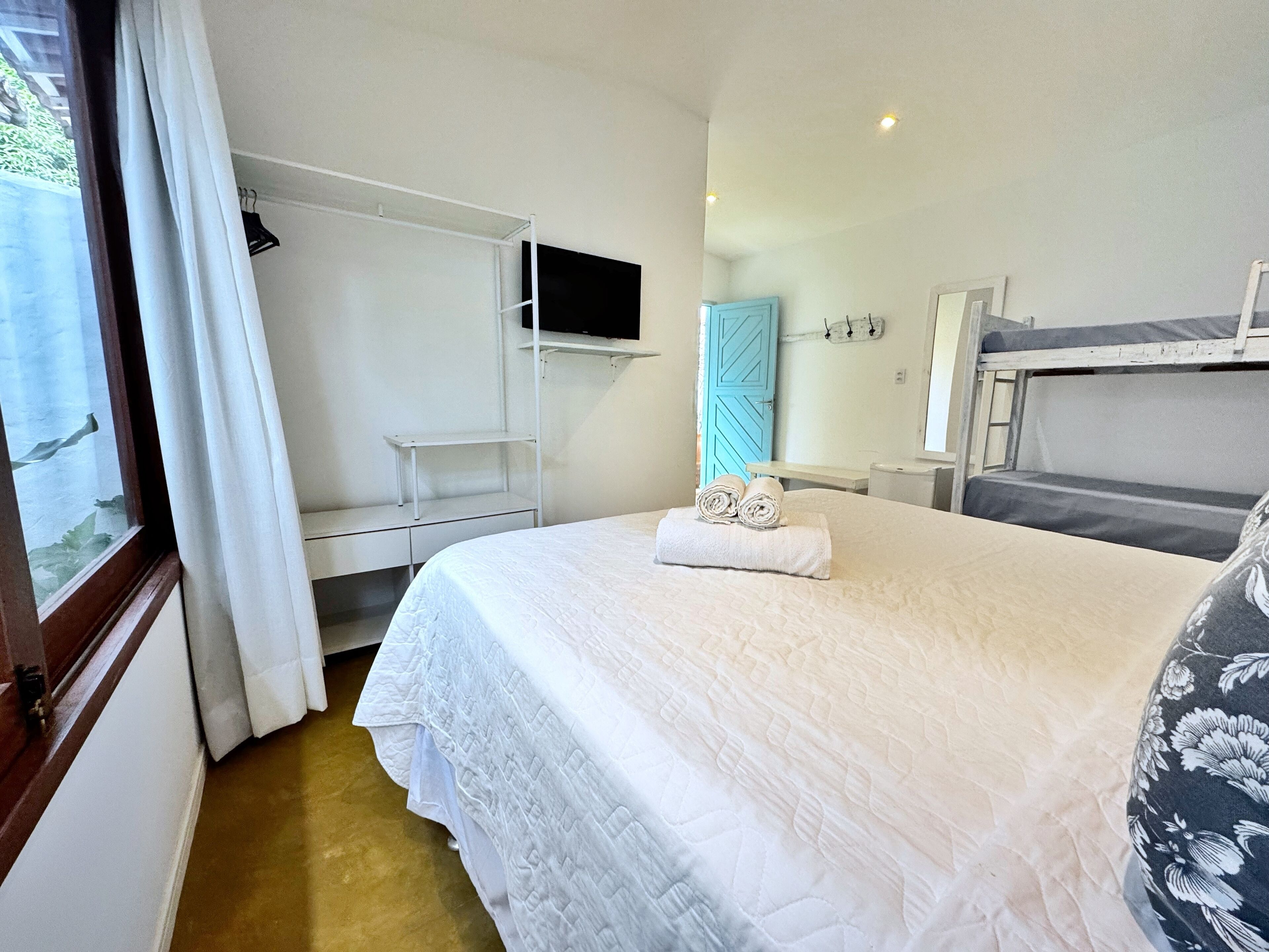 A neatly arranged bedroom with a bed, a TV mounted on the wall, a wardrobe, and a window with curtains.