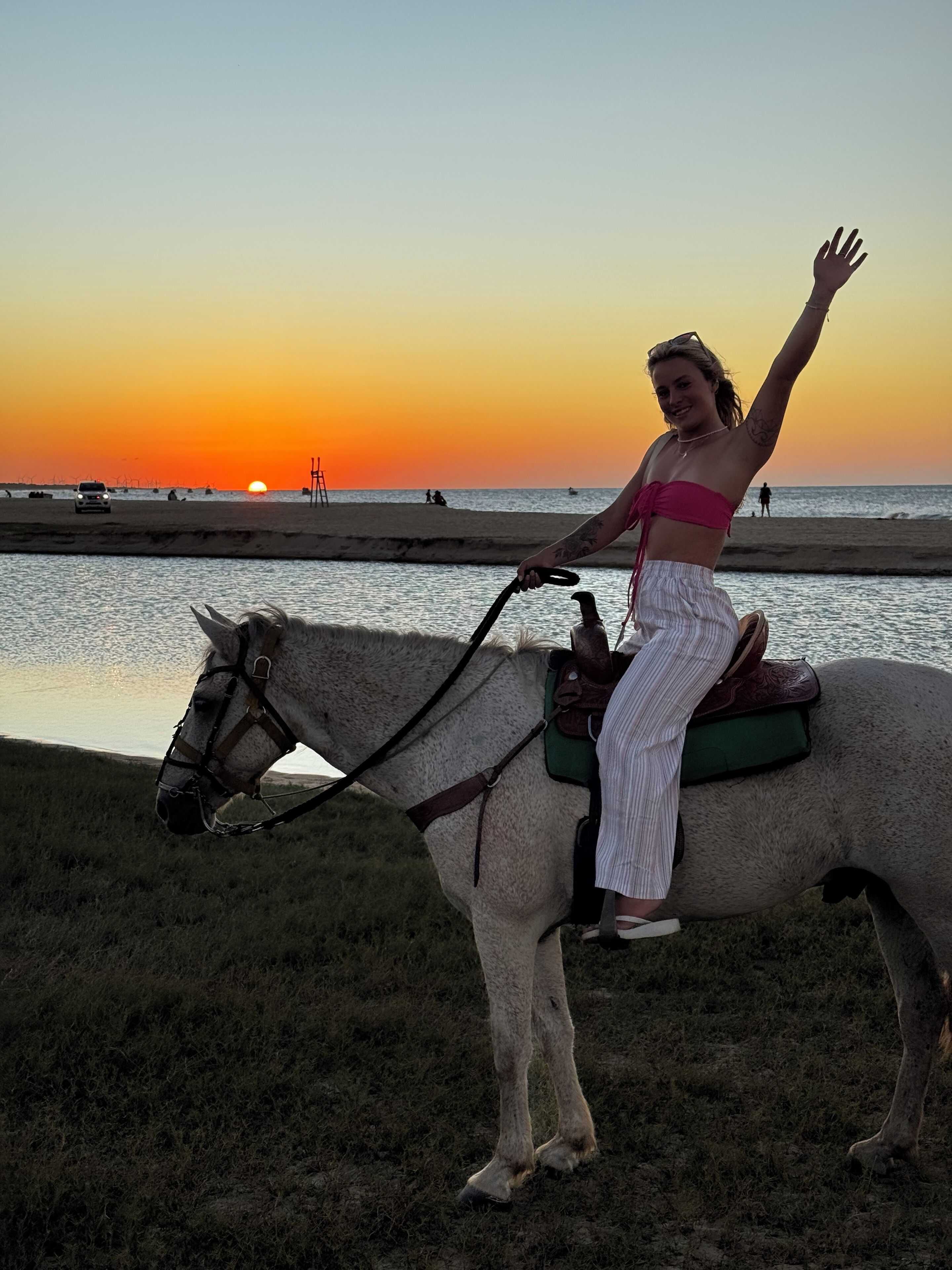 A person riding a horse with a saddle, near a body of water during sunset.