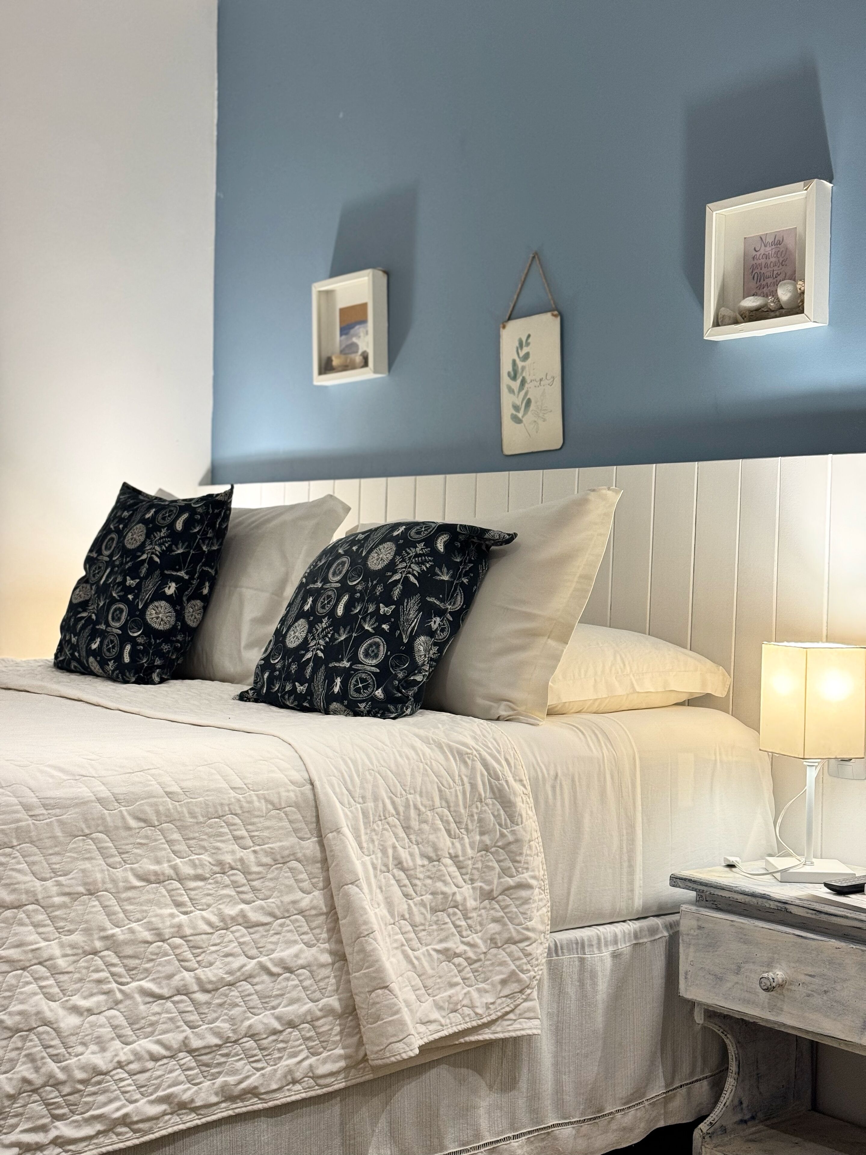 Een keurig opgemaakt bed met gestreepte kussens, een bedlamp en een klein nachtkastje.