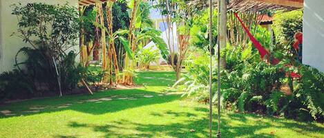 A lush garden with a swing, a hammock, and a variety of plants and trees.