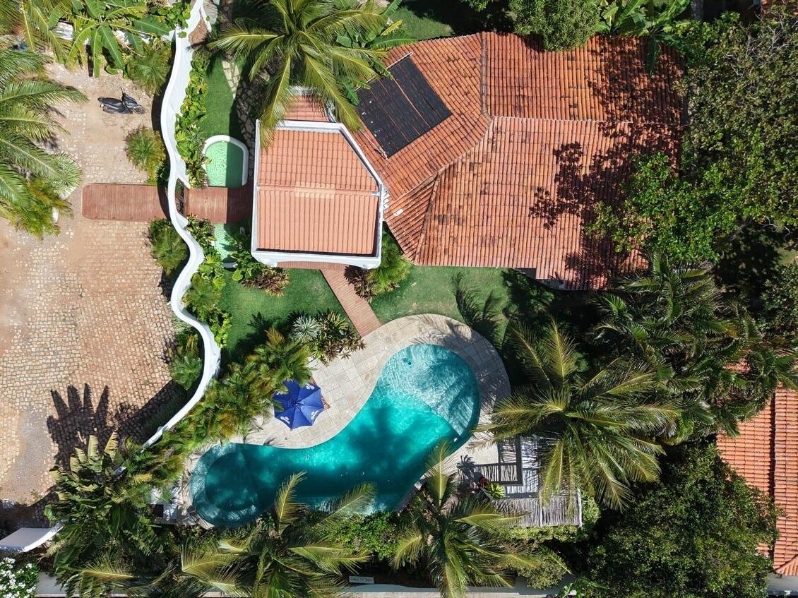 An aerial view of a resort with a swimming pool, palm trees, and a building with a tiled roof.