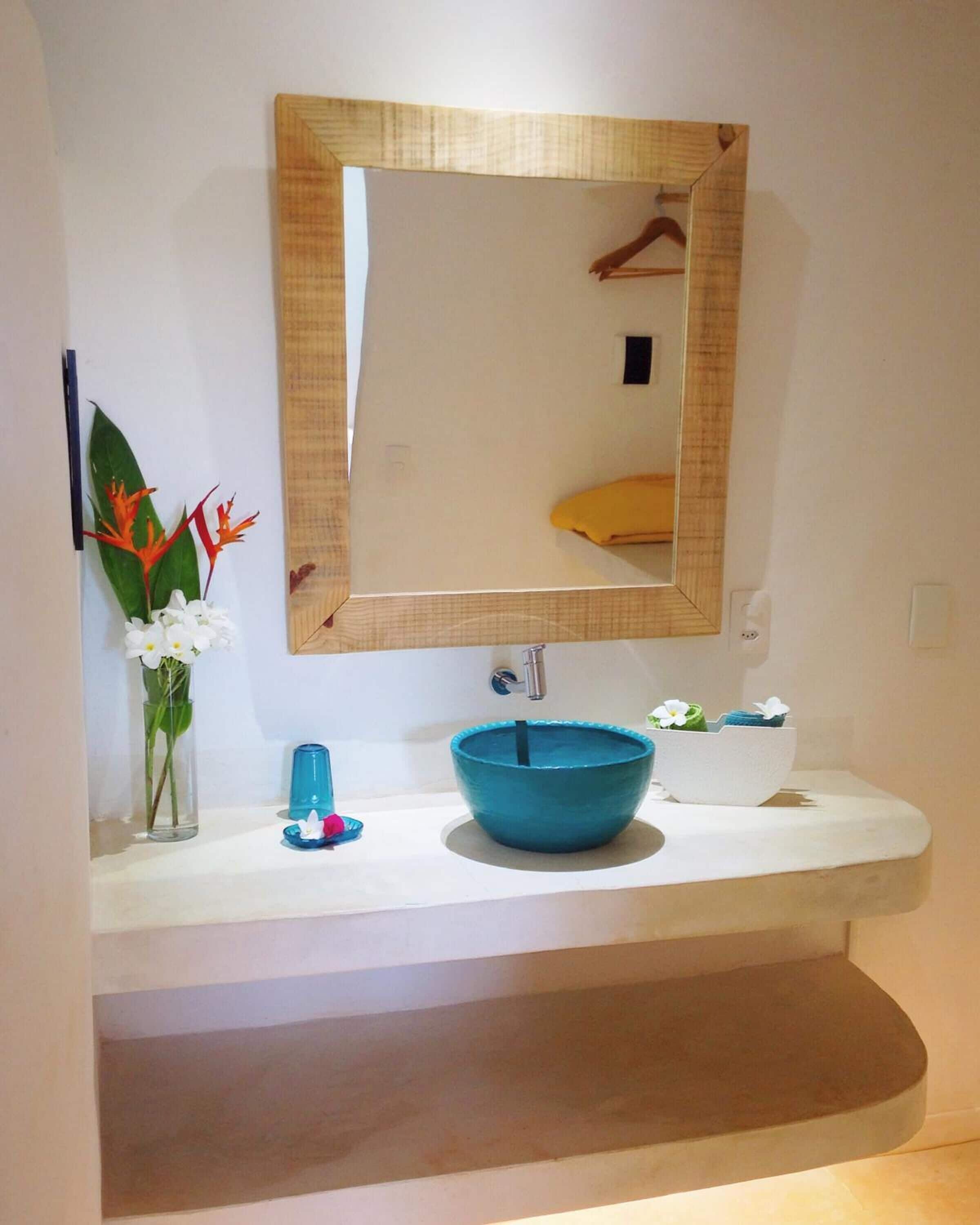 Un baño con un lavabo blanco, un cuenco azul, un espejo y un florero con flores.