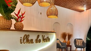 A reception area with a curved white counter, wooden ceiling, and hanging wicker lamps. - Pousada Ilha do Vento (São Miguel do Gostoso)