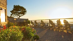 A beachfront patio with Adirondack chairs, a stone wall, and a tree. - Land's End at Cannon Beach (Cannon Beach)