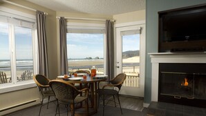 A dining area with a view of the beach, a fireplace, and wicker chairs. - Land's End at Cannon Beach (Cannon Beach)