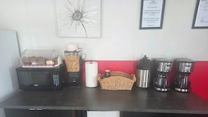 Una barra de desayuno con microondas, cafetera y recipiente para cereales.