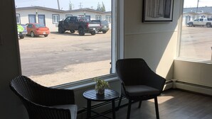 Una habitación con dos sillones de mimbre, una mesita con una planta y vista a un estacionamiento con vehículos.