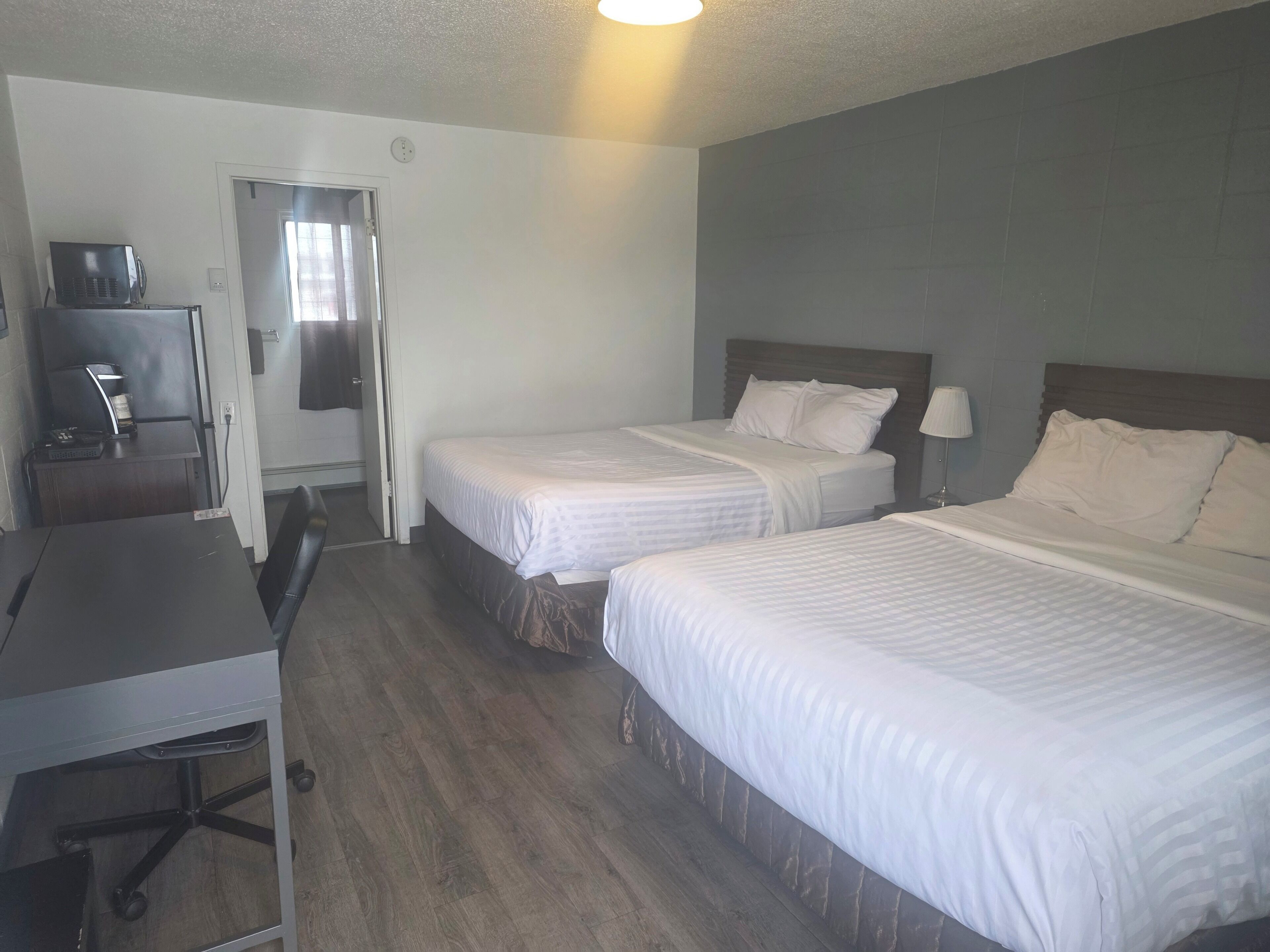 A hotel room with two beds, a desk, a chair, and a television.