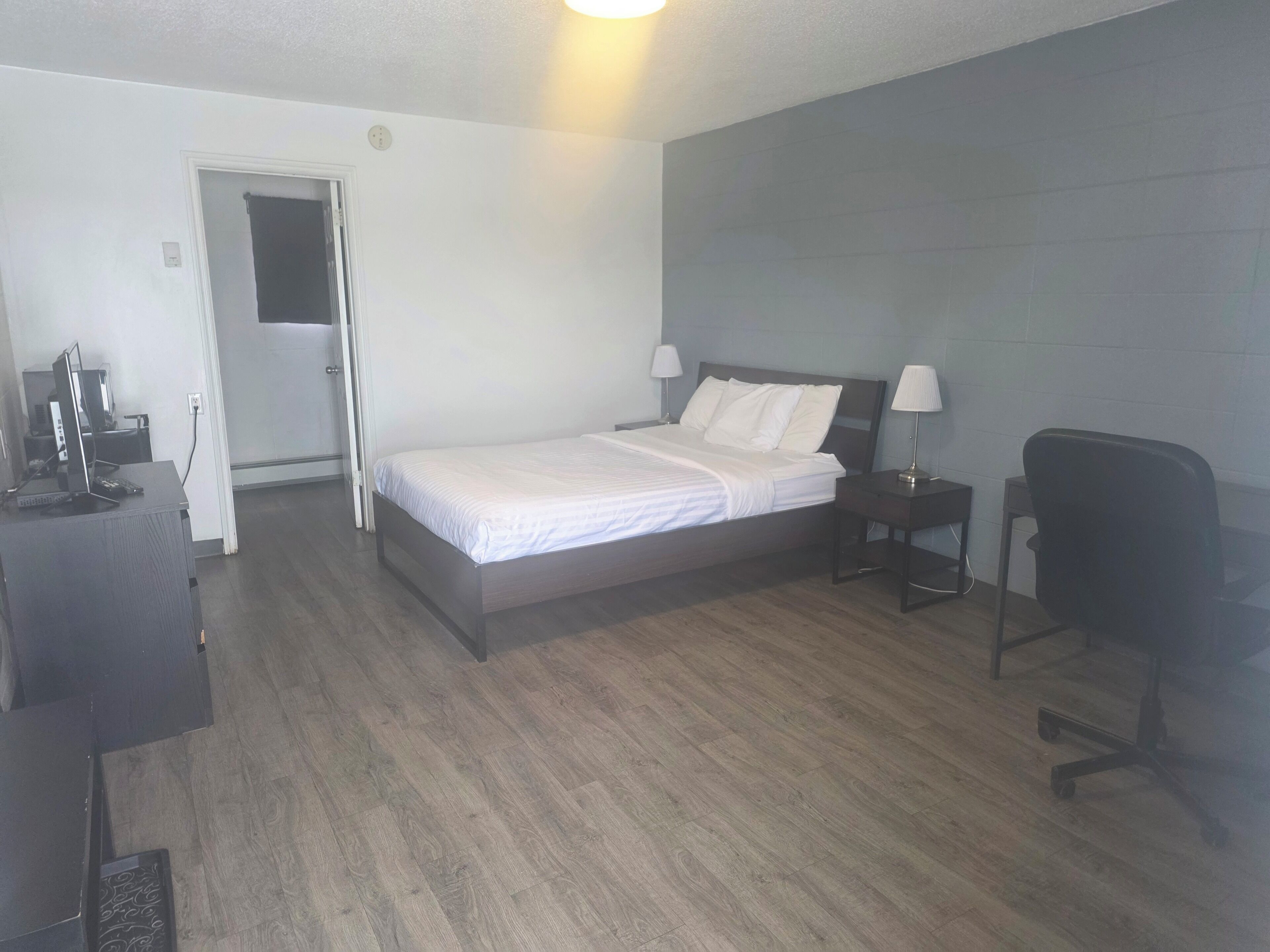 Quarto com cama, mesas de cabeceira, escrivaninha, cadeira e porta.