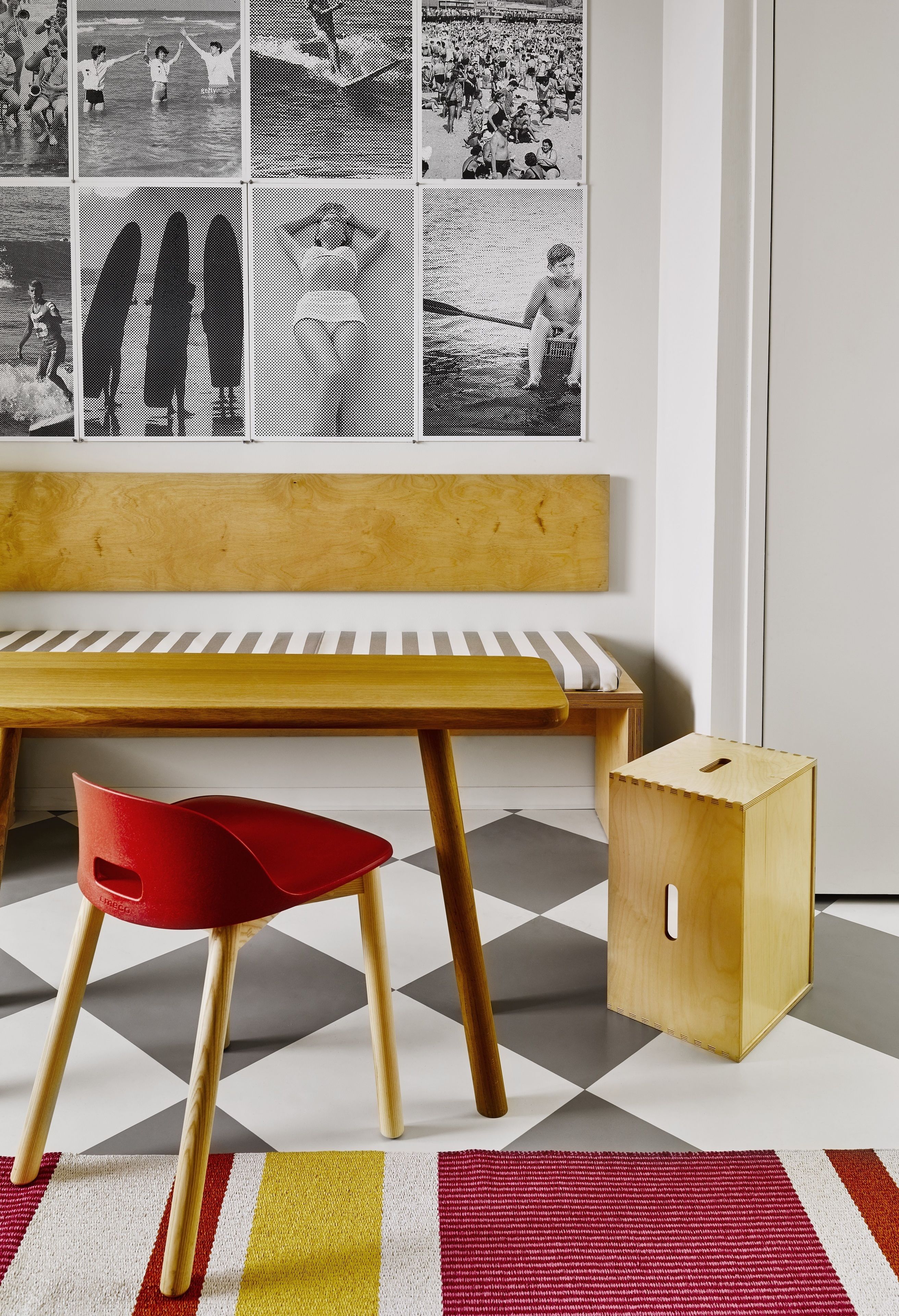Una habitación con un banco de madera, una silla roja, un mueble pequeño de madera y un suelo de cuadros.