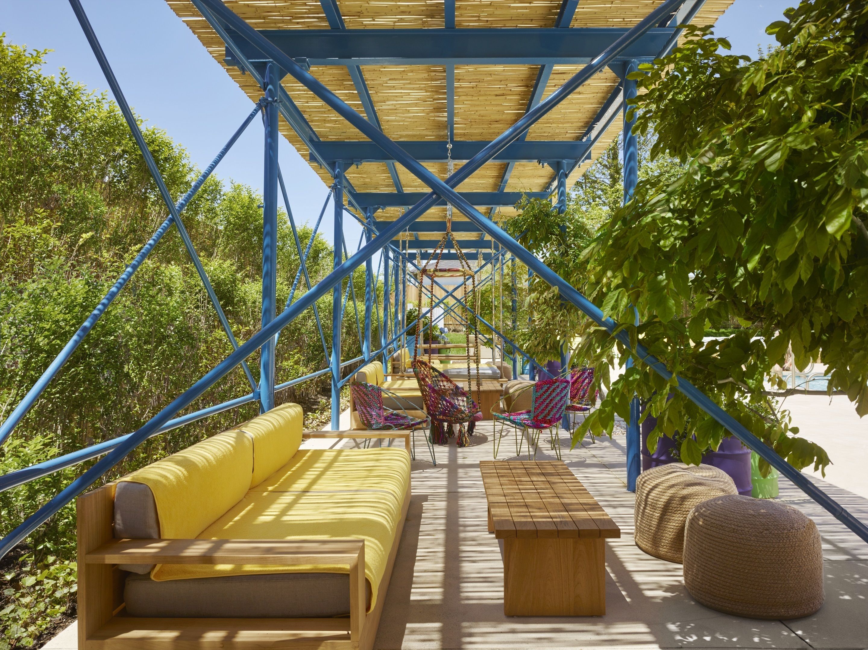 A covered outdoor seating area with a yellow sofa, colorful chairs, and a wooden table.