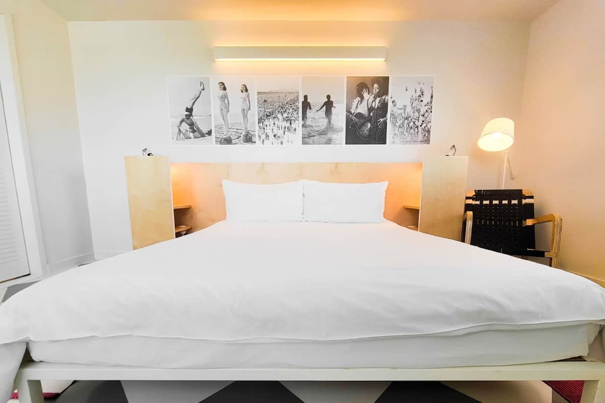 A hotel room with a large bed, a headboard with wall art, bedside lamps, and a checkered floor.