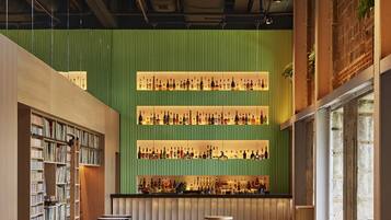 Une bibliothèque moderne avec des étagères, un coin bar avec des bouteilles, ainsi que des tables et des bancs en bois.