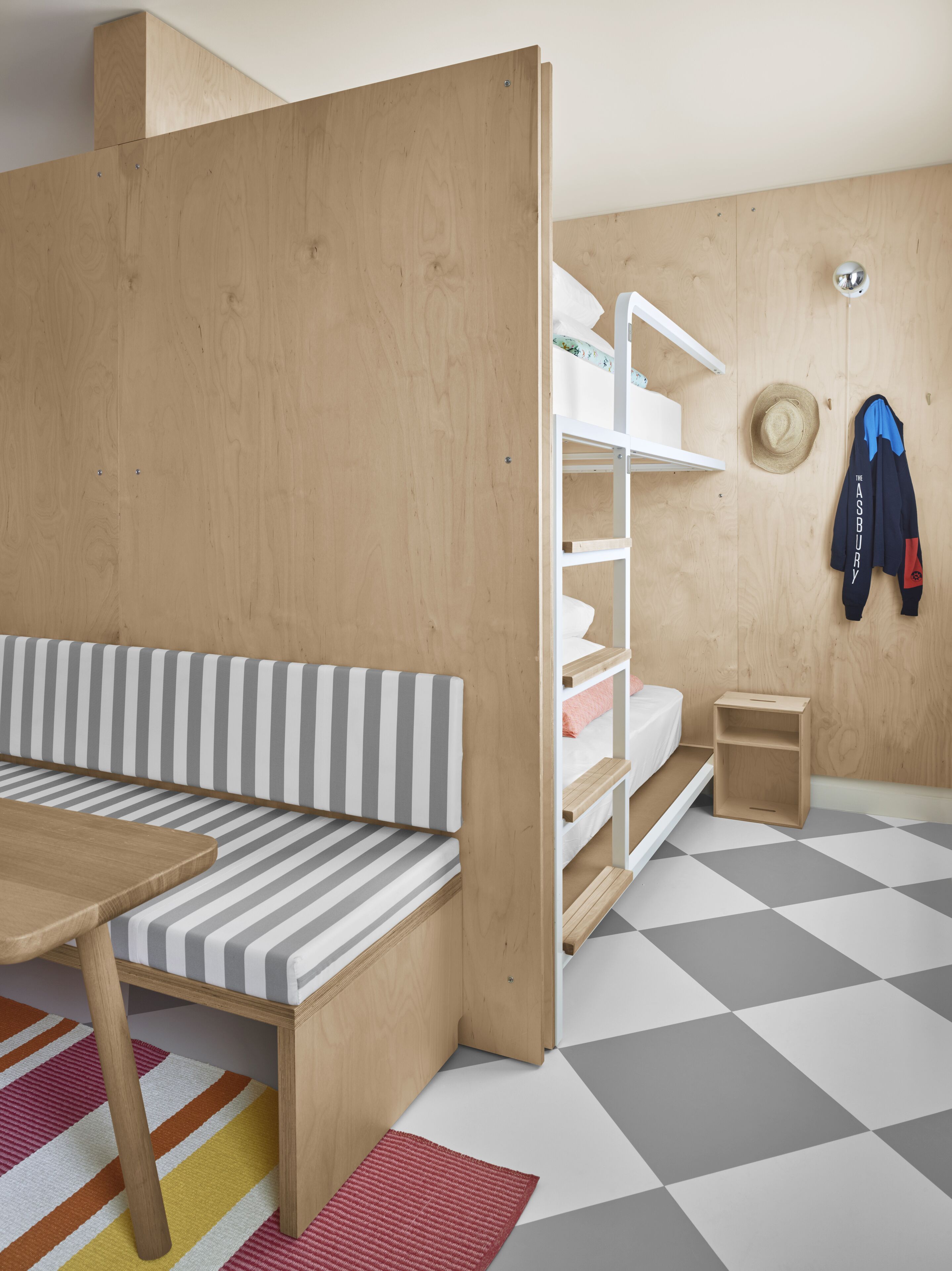 Una habitación con un banco a rayas, un armario de madera, un estante blanco y un suelo de cuadros.