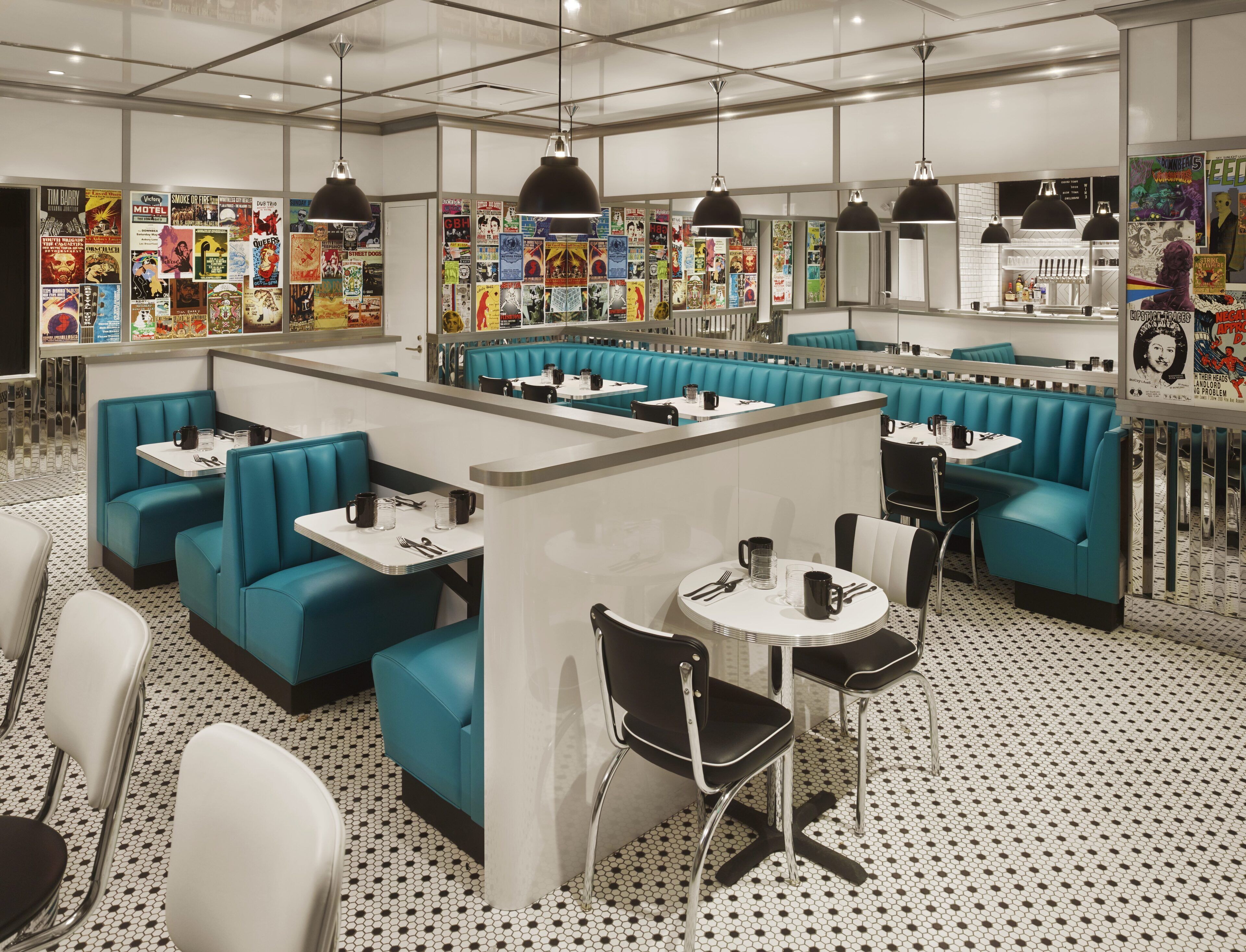 Un restaurante con asientos tapizados en tono aguamarina, mesas blancas y una pared decorada con carteles antiguos.