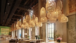A spacious indoor area with wooden tables and benches, large windows, and hanging woven light fixtures. - The Asbury Hotel (Asbury Park)