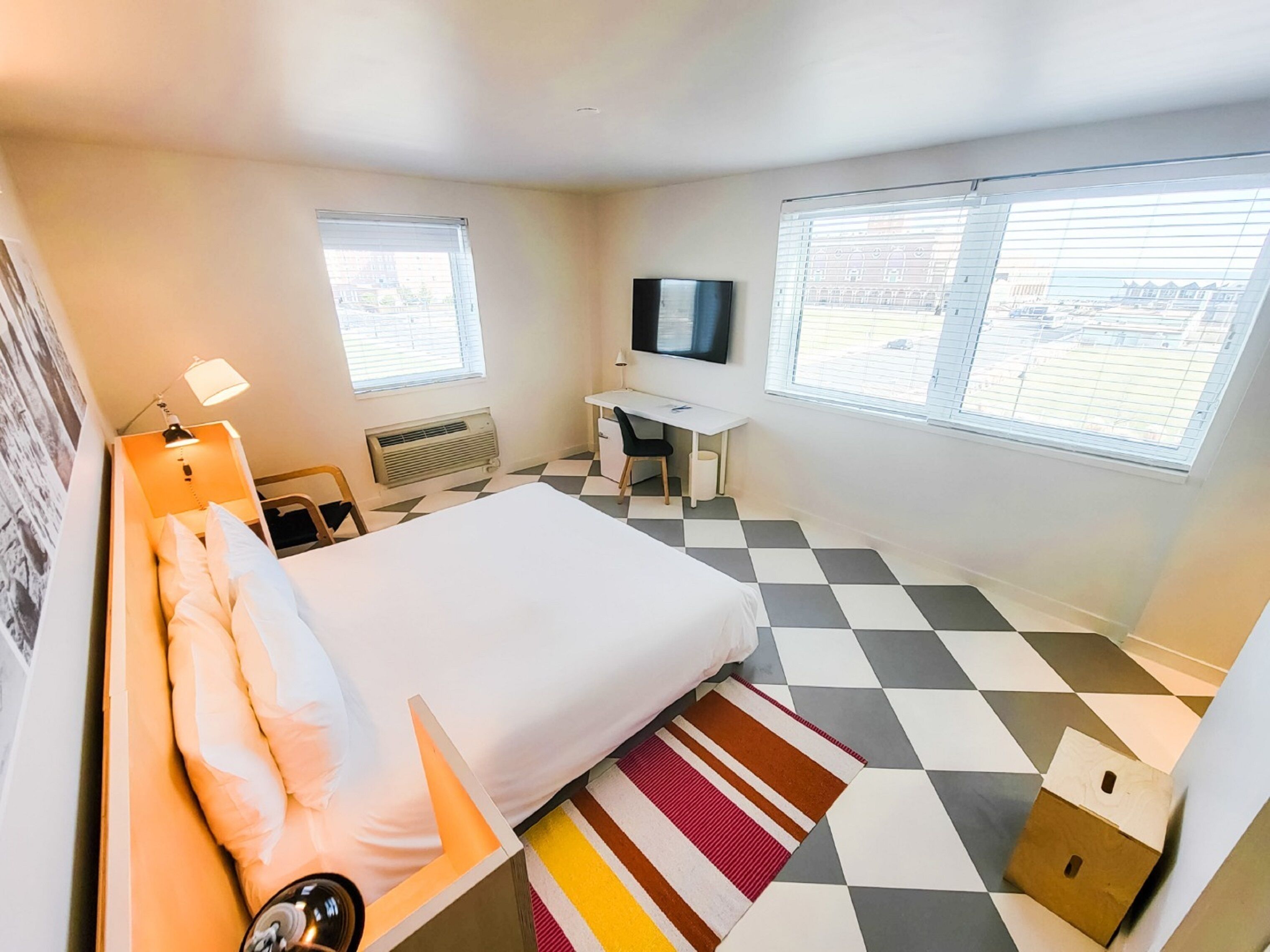 Une chambre d’hôtel avec un lit, un bureau, une chaise, une télévision et deux fenêtres.