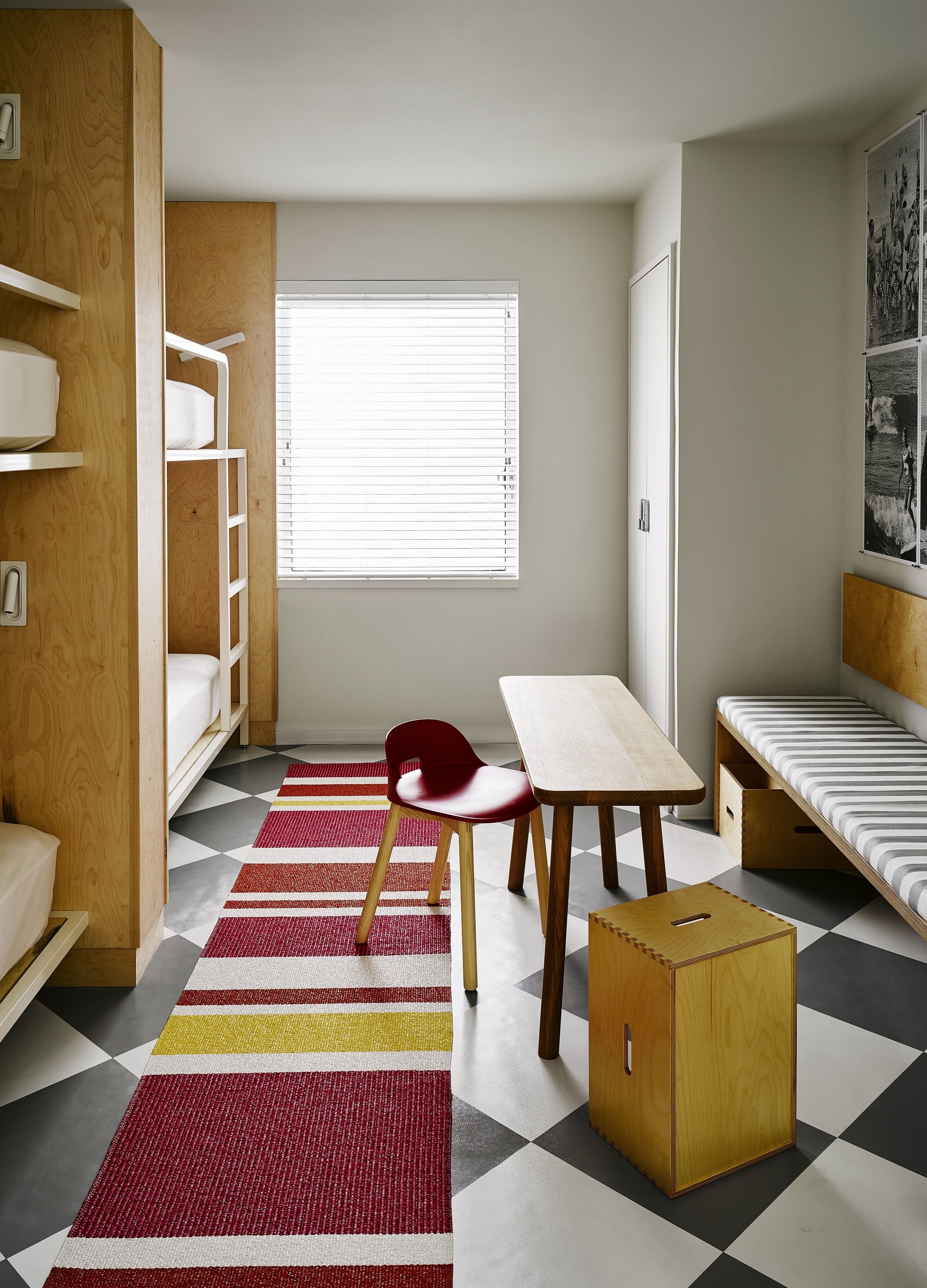 Une chambre à coucher de taille modeste, comprenant un lit superposé, un lit simple, un bureau en bois, une chaise et une petite table.