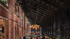 A spacious lounge area with a long bench seating arrangement, a brick wall on one side, and large windows on the other. - The Asbury Hotel (Asbury Park)