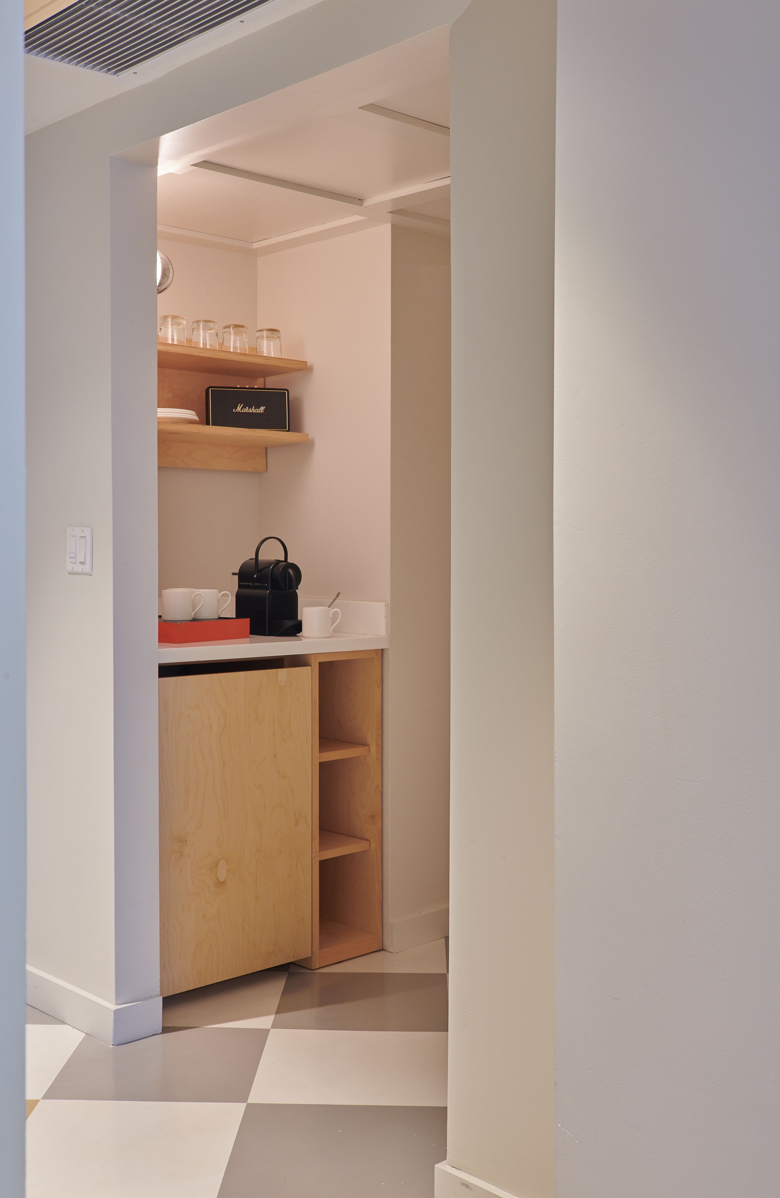 Un couloir étroit avec un coin cuisine comprenant un meuble en bois, un plan de travail et une étagère avec des bocaux en verre et une bouilloire.