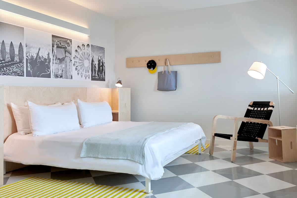 A modern hotel room with a large bed, a desk, a chair, and a desk lamp.