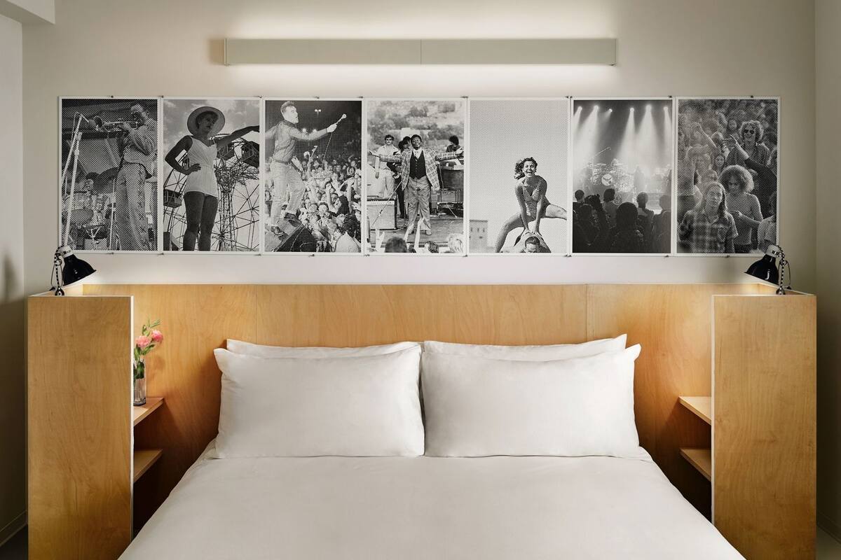 A hotel room with a wooden headboard, a large bed with white linens, and a wall-mounted photo display.