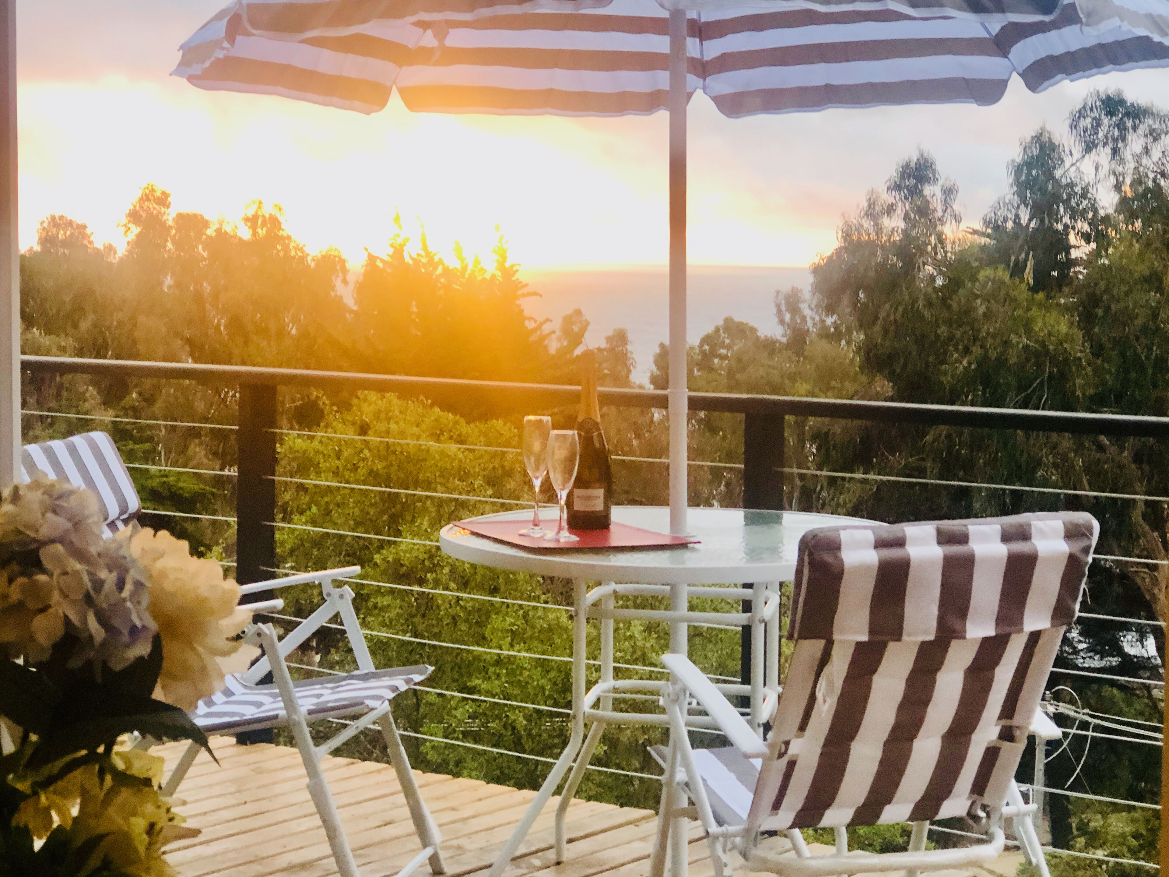 Une terrasse avec une table et des chaises, une bouteille de vin et un parasol.