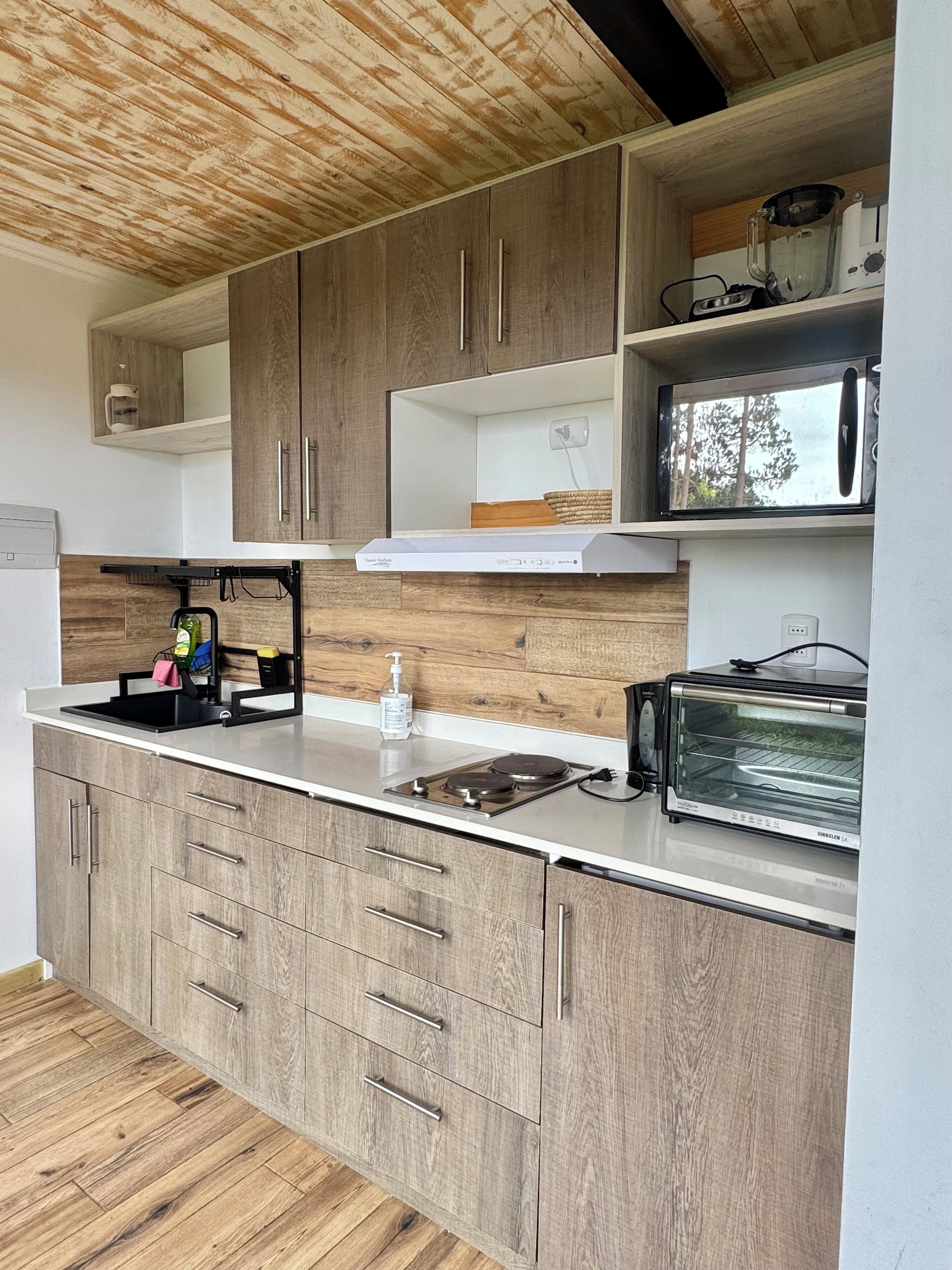 A modern kitchen with wooden cabinets, a built-in stove, a microwave, and a coffee machine.