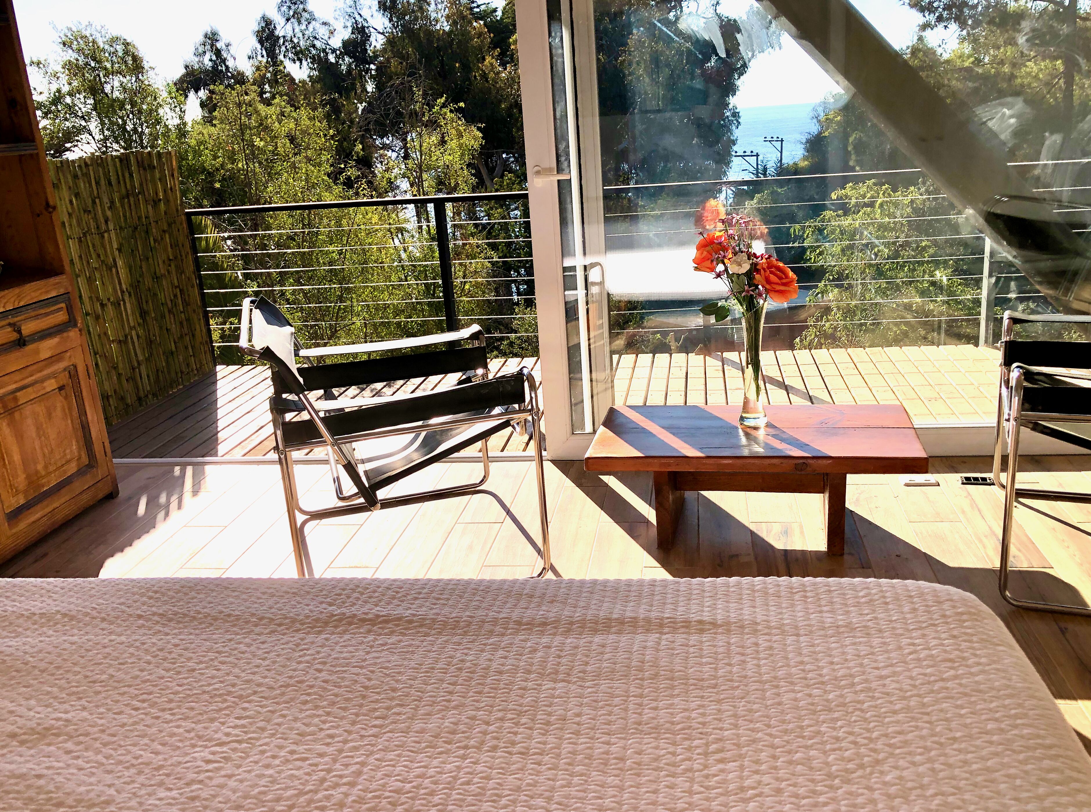 Un balcón con una mesa de madera, un banco y un florero con flores.