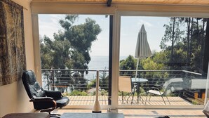 Ein modernes Wohnzimmer mit einem großen Fenster mit Blick auf eine Terrasse und das Meer.