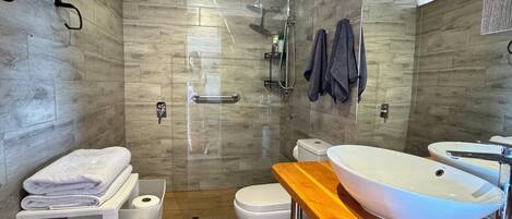 A modern bathroom with a wooden floor, a large white sink, a toilet, and a shower area.