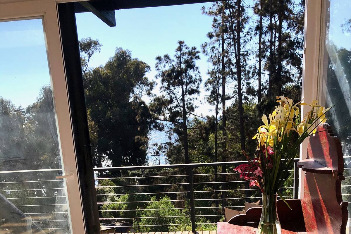 Une pièce dotée d’une grande porte-fenêtre coulissante donnant sur une terrasse extérieure. On y trouve une table en bois sur laquelle est posé un vase rempli de fleurs.