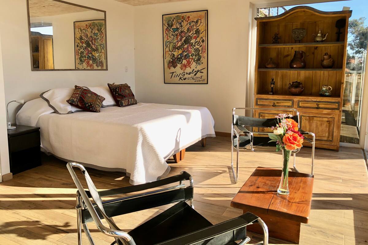 Une chambre à coucher comprenant un lit, une armoire en bois agrémentée d’objets décoratifs, une chaise et une table sur laquelle est posé un vase de fleurs.