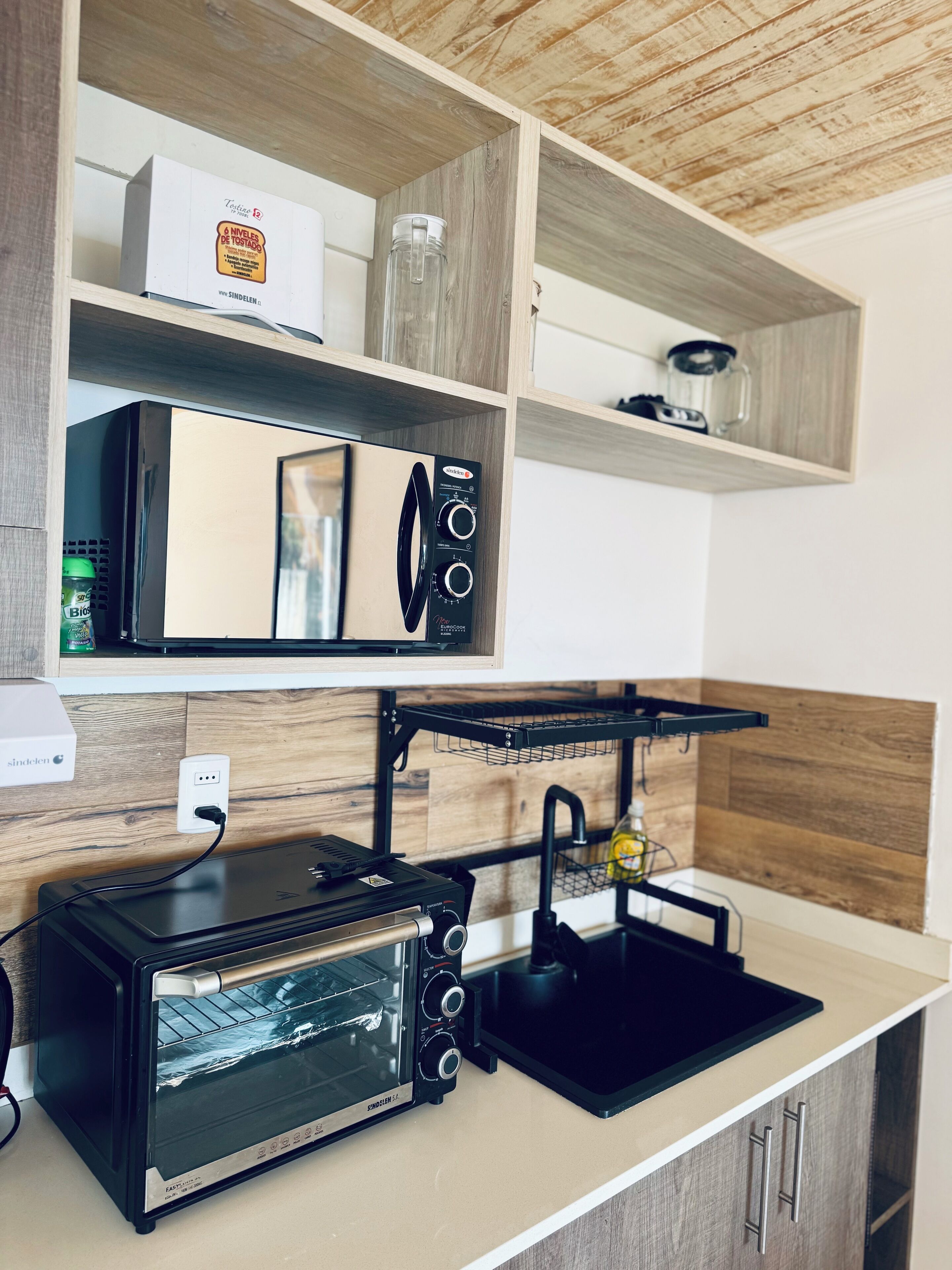 A modern kitchen with a built-in oven, microwave, and toaster. There is a shelf with a box of bread and a bottle of olive oil.