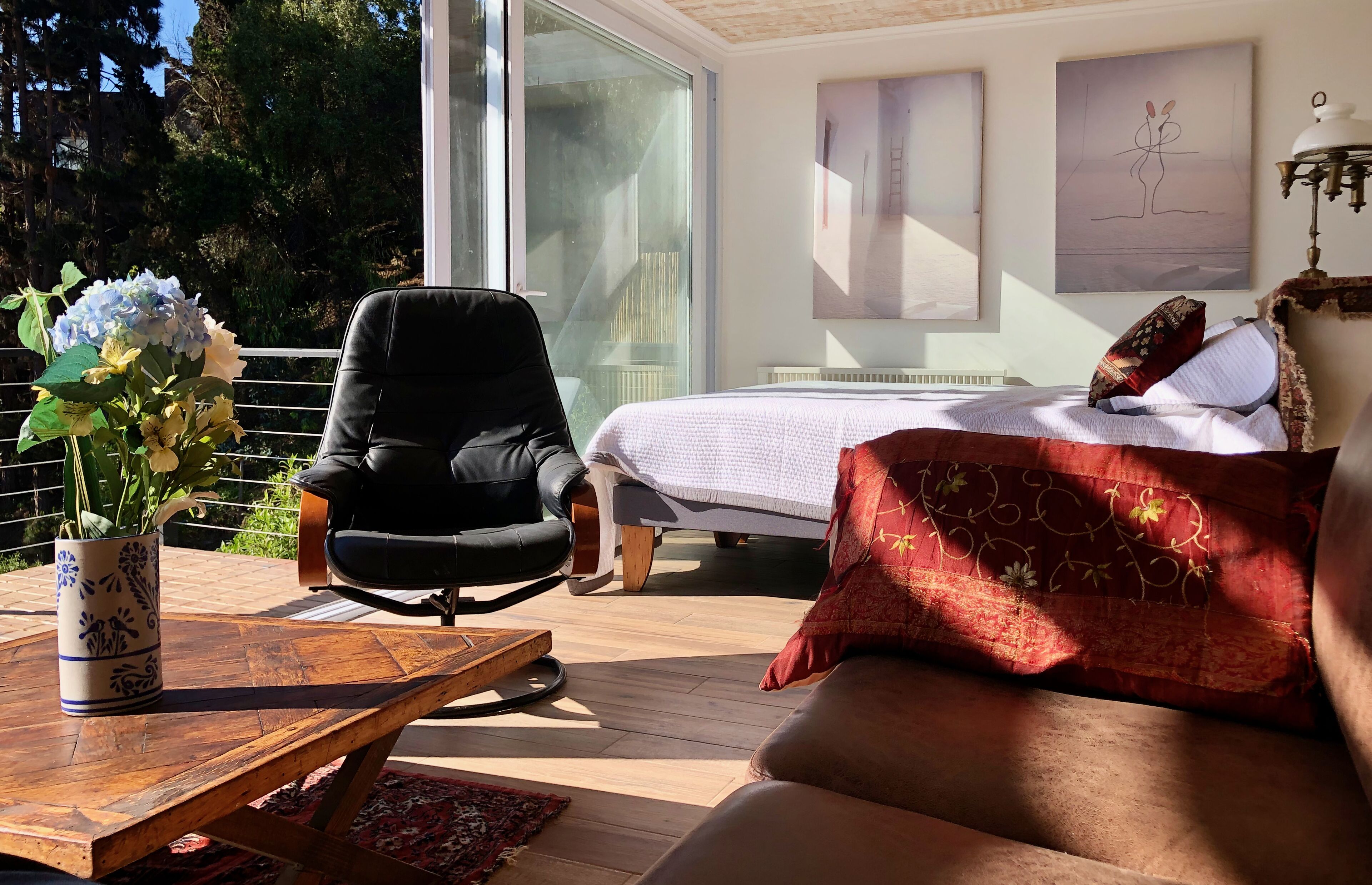 A bedroom with a bed, a chair, a table with a vase of flowers, and a view of the outdoors.