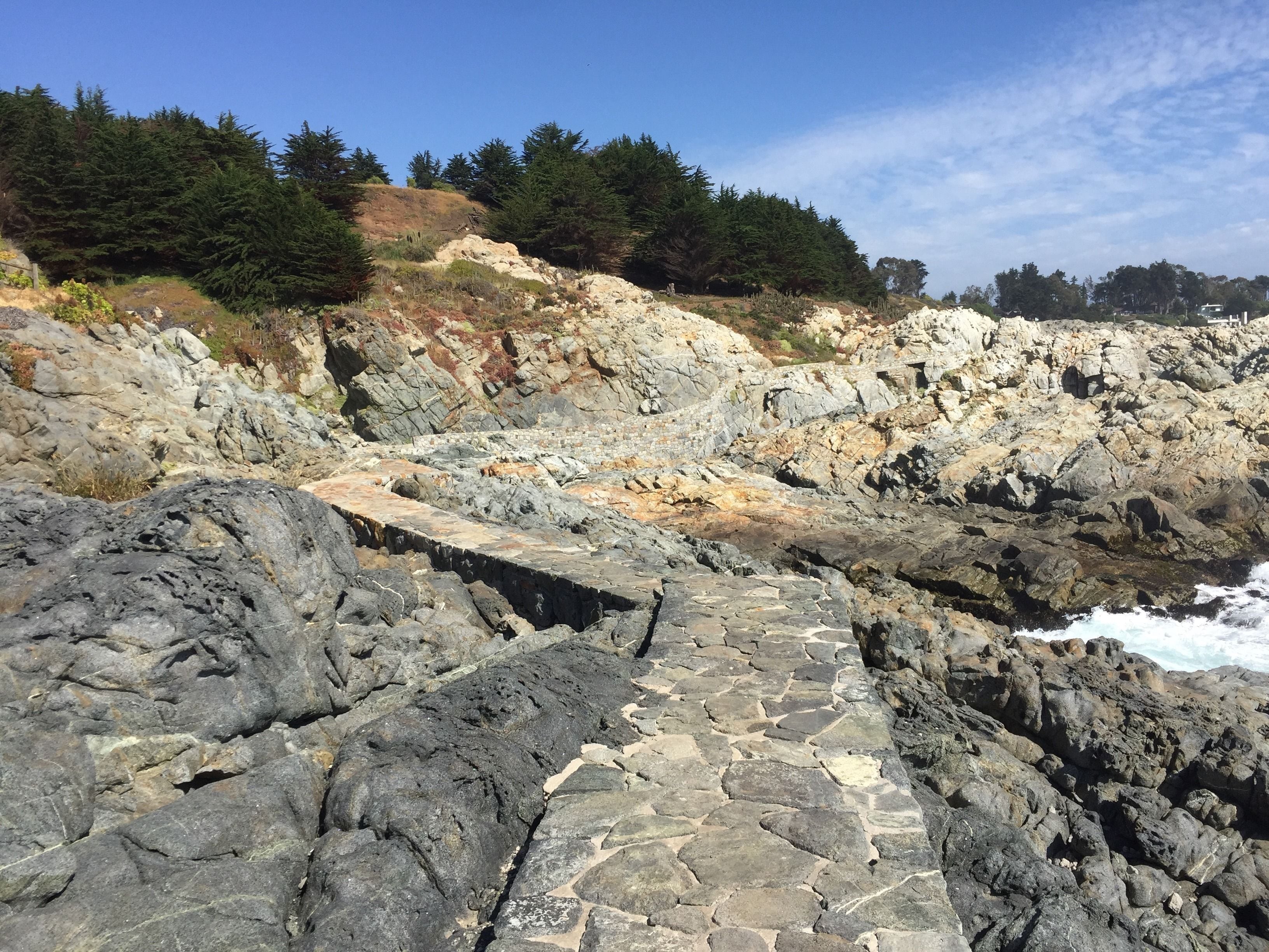 A rocky coastal path with a stone bridge leading to a cliff edge.