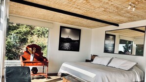 Ein modernes Schlafzimmer mit einem großen Bett, Holzboden und Blick auf Grün.