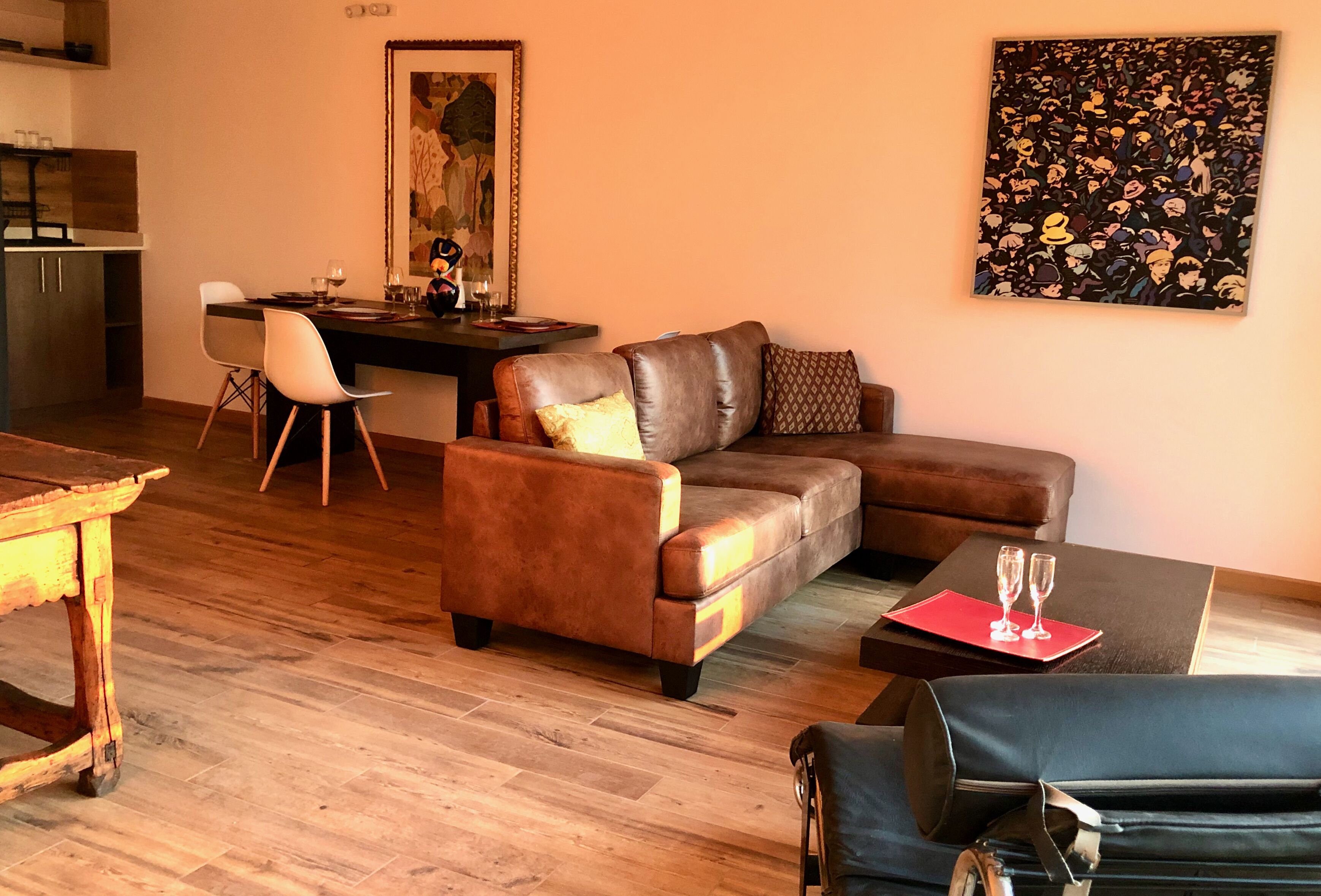 A living room with a brown leather sofa, a dining table with chairs, a black coffee table, and a painting on the wall.
