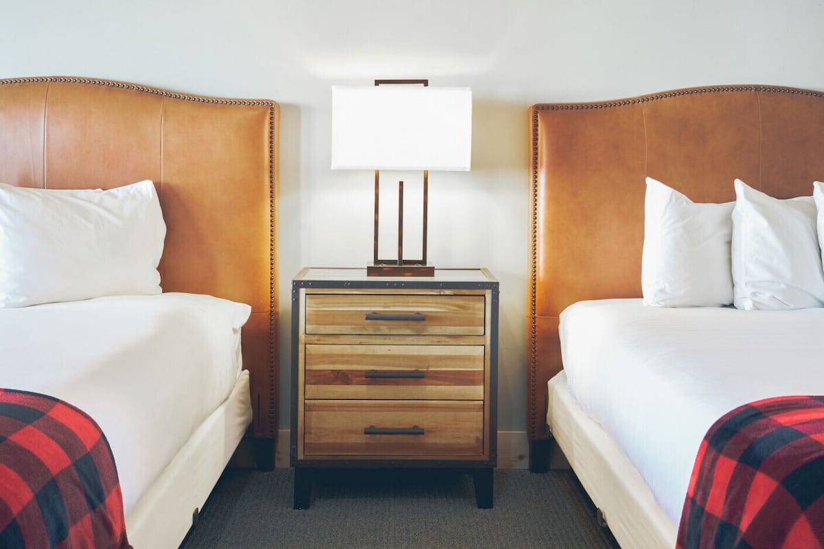 A hotel room with two beds, a nightstand with a lamp, and a wooden dresser.