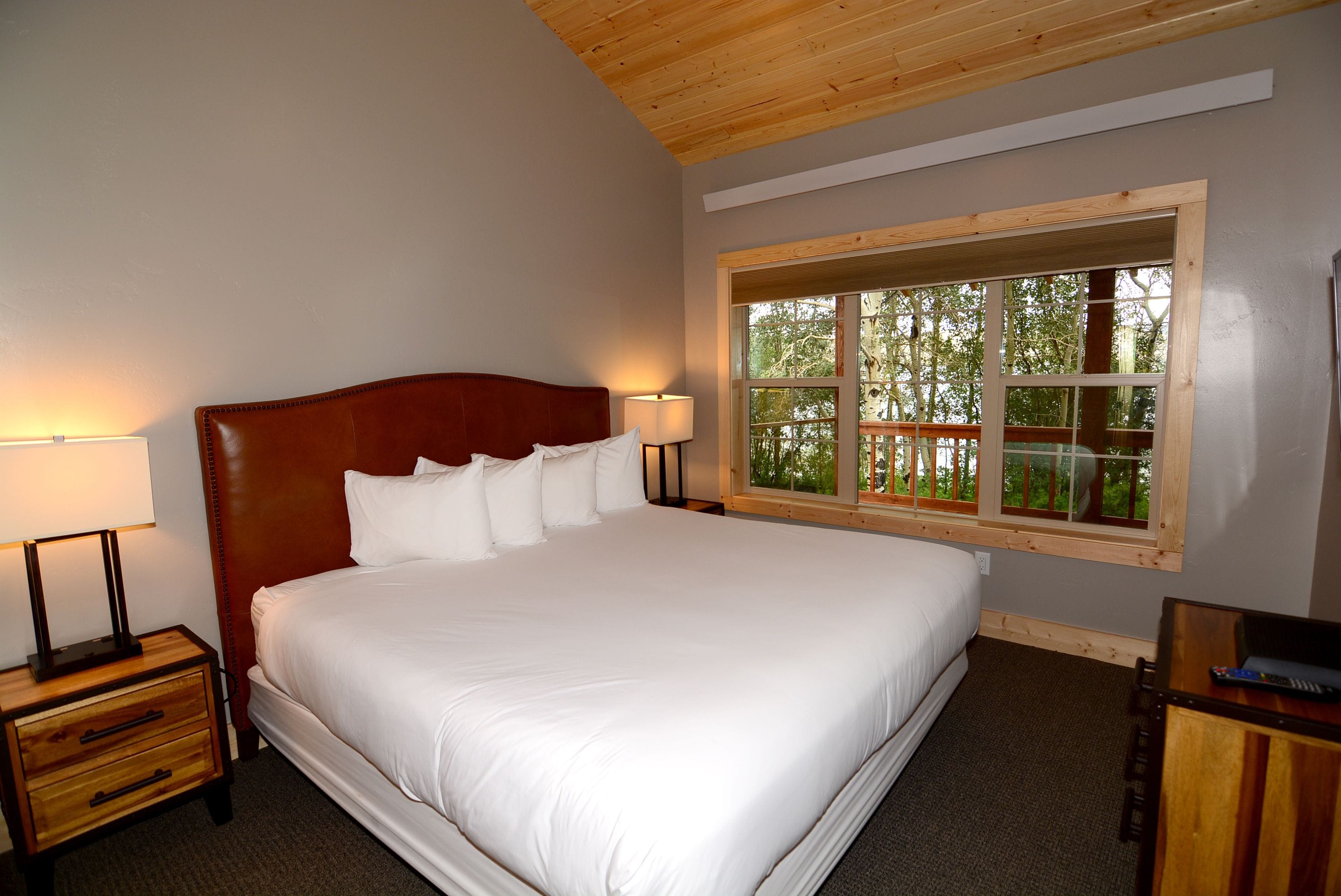 A neatly made bed with white linens, a wooden headboard, and two bedside lamps.
