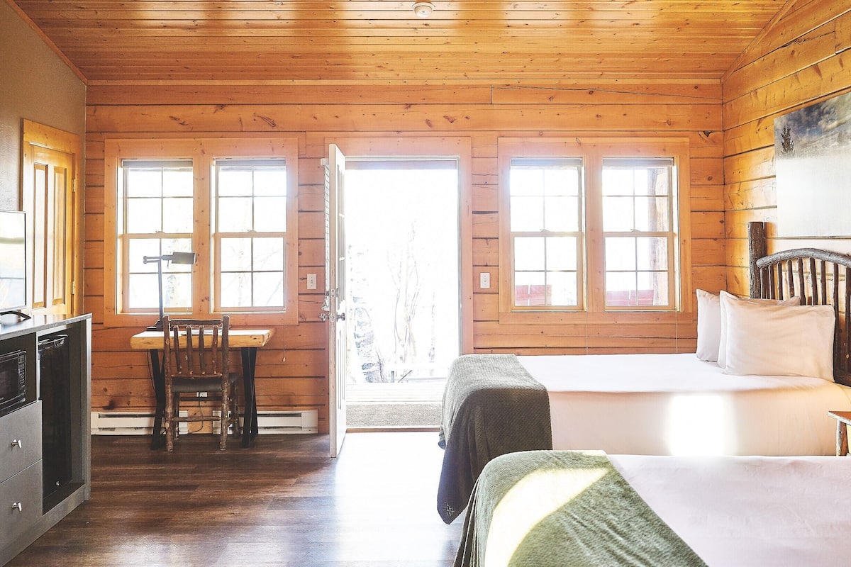 A wooden cabin room with a bed, a desk, and a chair.
