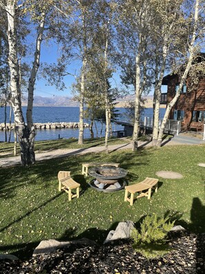 A lakeside outdoor seating area with a fire pit, wooden benches, and a view of the lake and mountains. - Lakeside Lodge Resort & Marina (Pinedale)