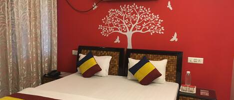 A hotel room with a large bed, two pillows, a nightstand, an air conditioning unit, and a wall with a tree decal.