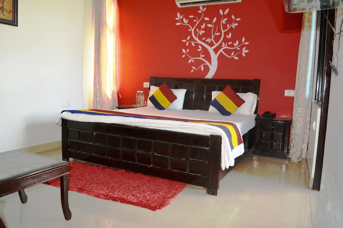 Un dormitorio con una cama, una alfombra roja, una mesita de noche y un mural de un árbol en la pared.