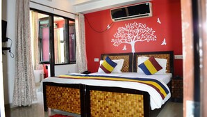 A bedroom with a bed, a red wall with a tree mural, and a window with curtains. - Blessings Jaipur (Jaipur)
