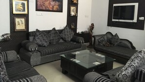 A living room with a sofa set, a coffee table, and wall-mounted decorations including framed pictures and a television. - Blessings Jaipur (Jaipur)