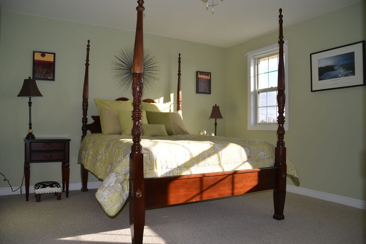 A four-poster bed with a floral bedspread, a nightstand with a lamp, and a small stool.