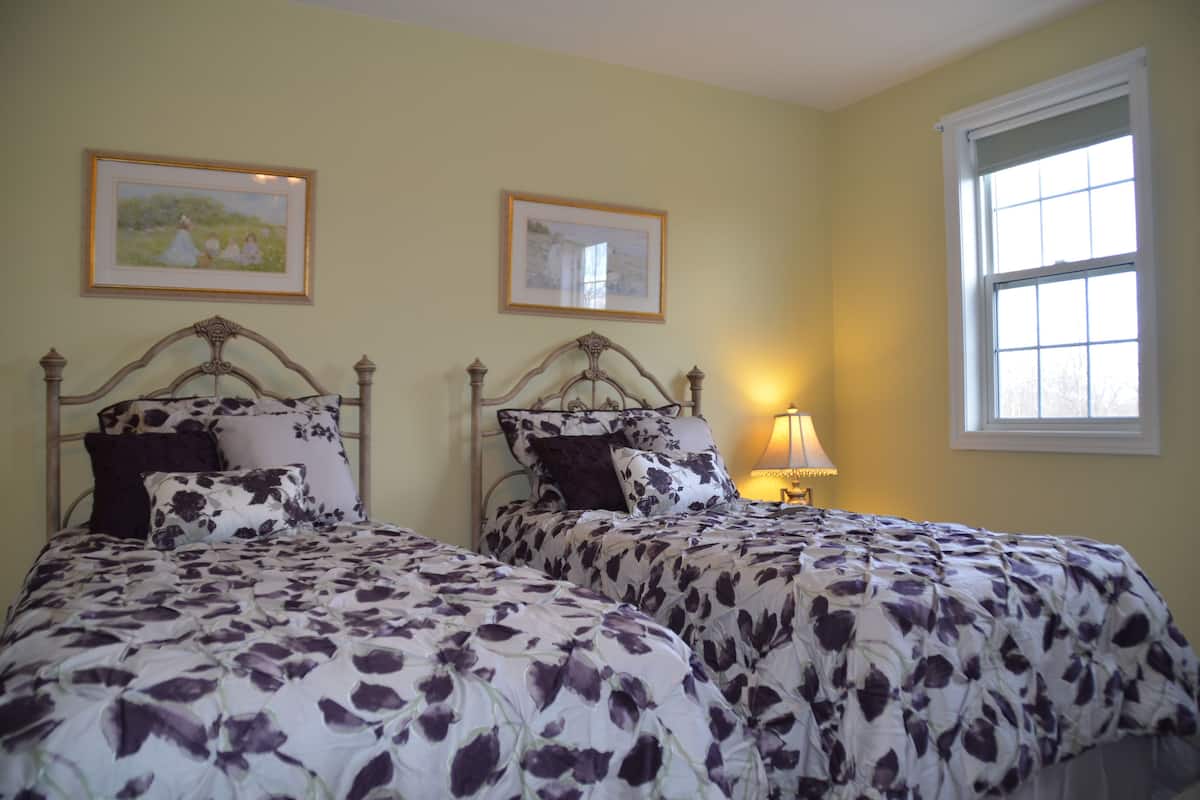 A bedroom with two beds, each with floral-patterned bedding, a bedside table with a lamp, and framed pictures on the wall.