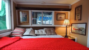 A hotel room with a large bed, a window with a view of boats, a lamp, and framed pictures on the wall. - MV GiaMaria (Richmond)