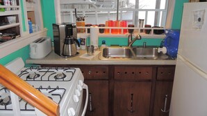 A kitchen with a stove, sink, and various appliances. There are cabinets, a window, and a shelf with items. - MV GiaMaria (Richmond)